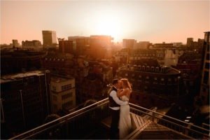 Bride and Groom kissing with the Manchester skyline in the background as the sun is setting