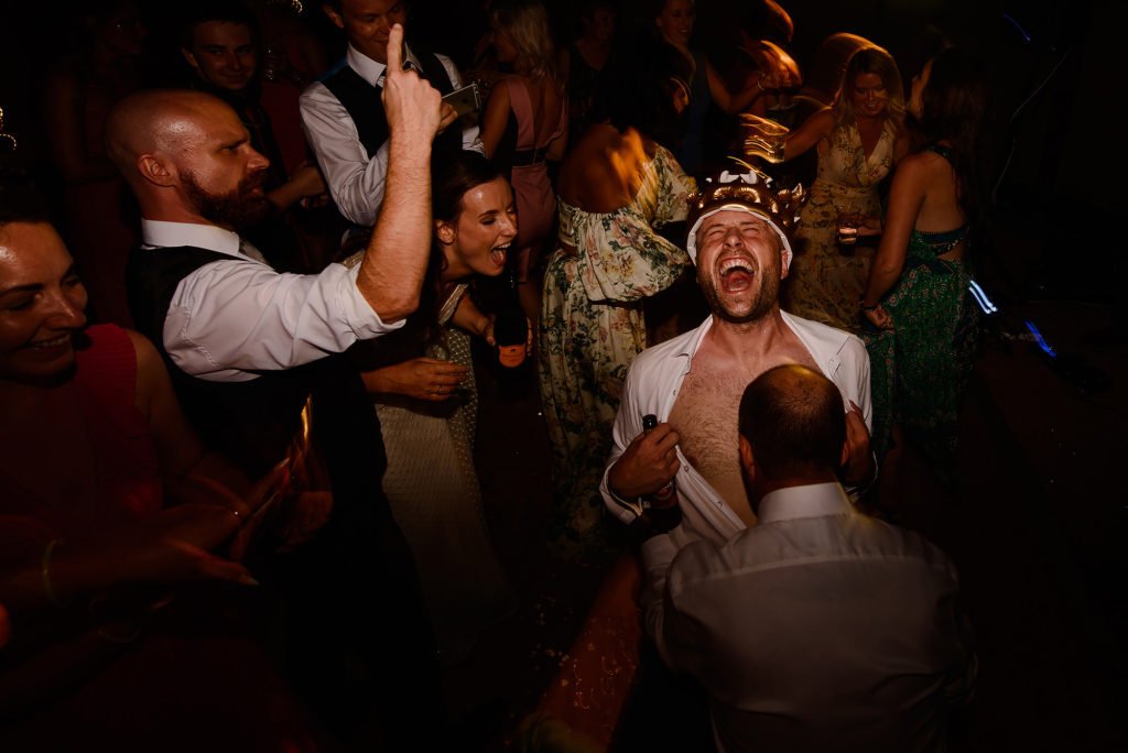 Groom with his shirt open, wearing a crown on the dance floor