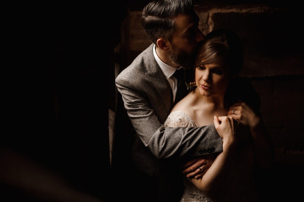 Groom with his arms around the Bride, kissing her on the head