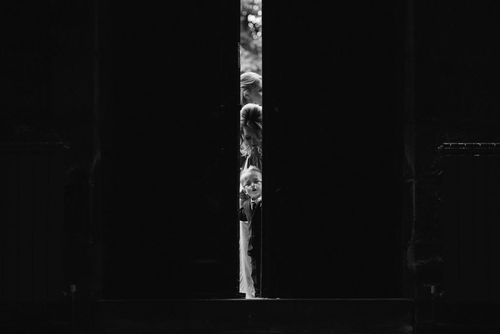 page boy peeking through the church doors before the wedding ceremony starts