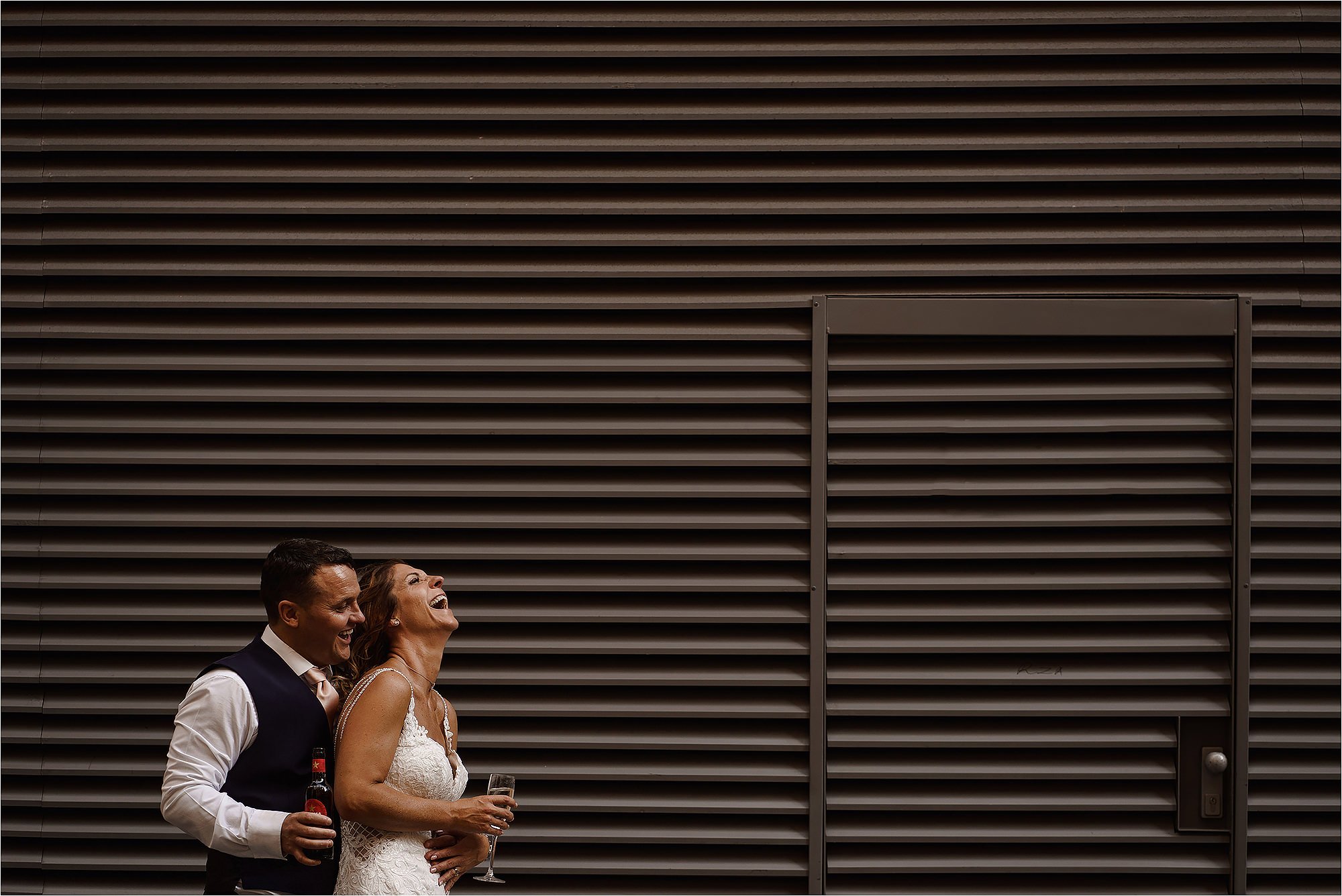 Bride and Groom laughing as they stand together in front of a metal vent