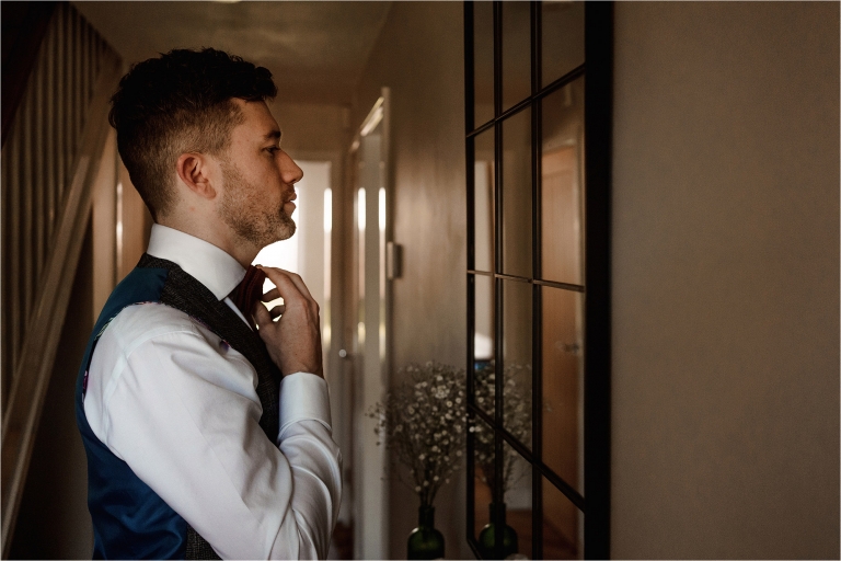 Groom tying his bow tie in the mirror