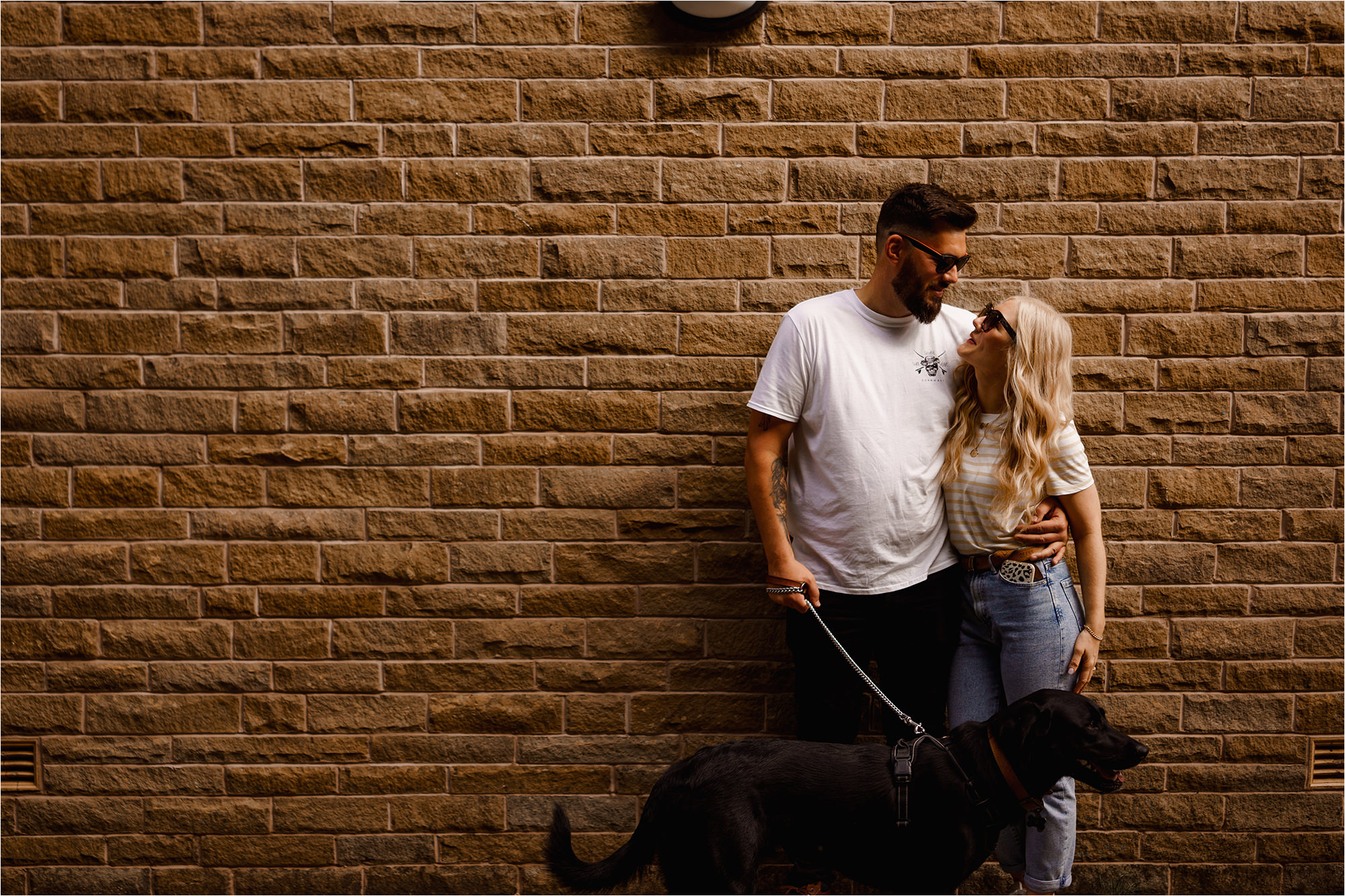 Photo of couple leaning against wall with their dog